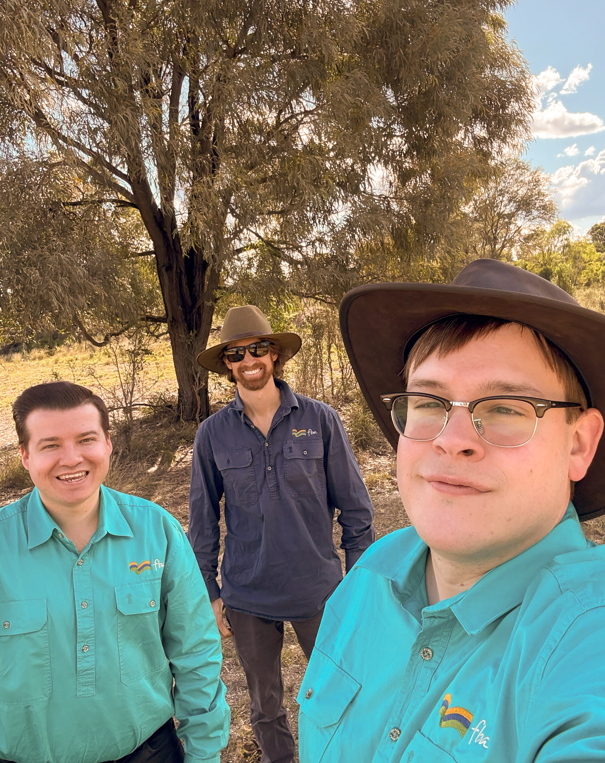 Three men standing out in a field taking a selfie.