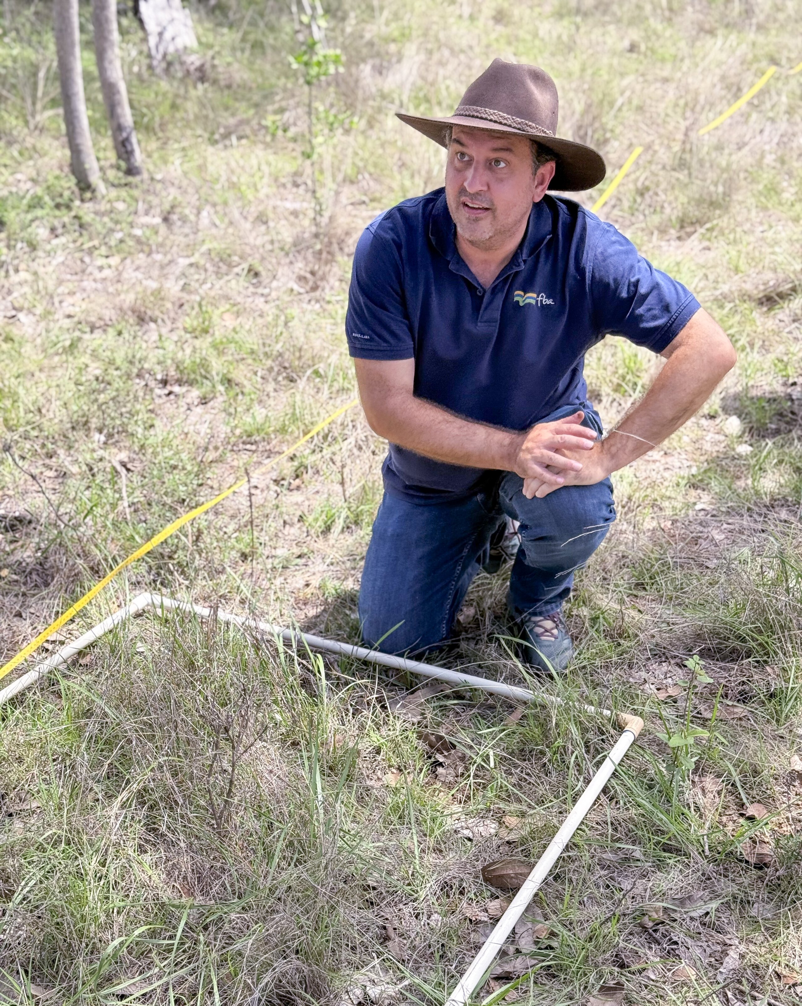 A man kneeling in a grass field marking an area