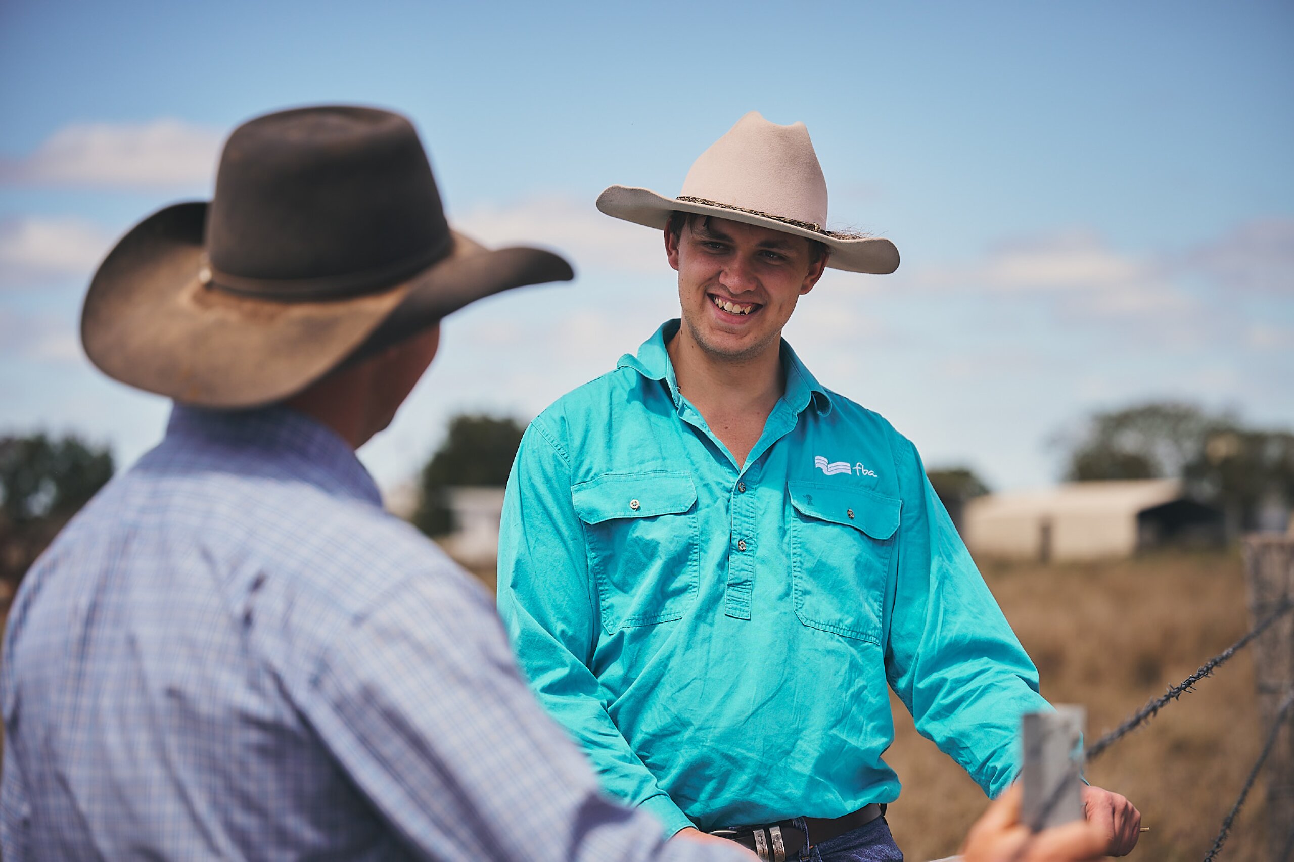 Two men talking and smiling while standing next to a fence