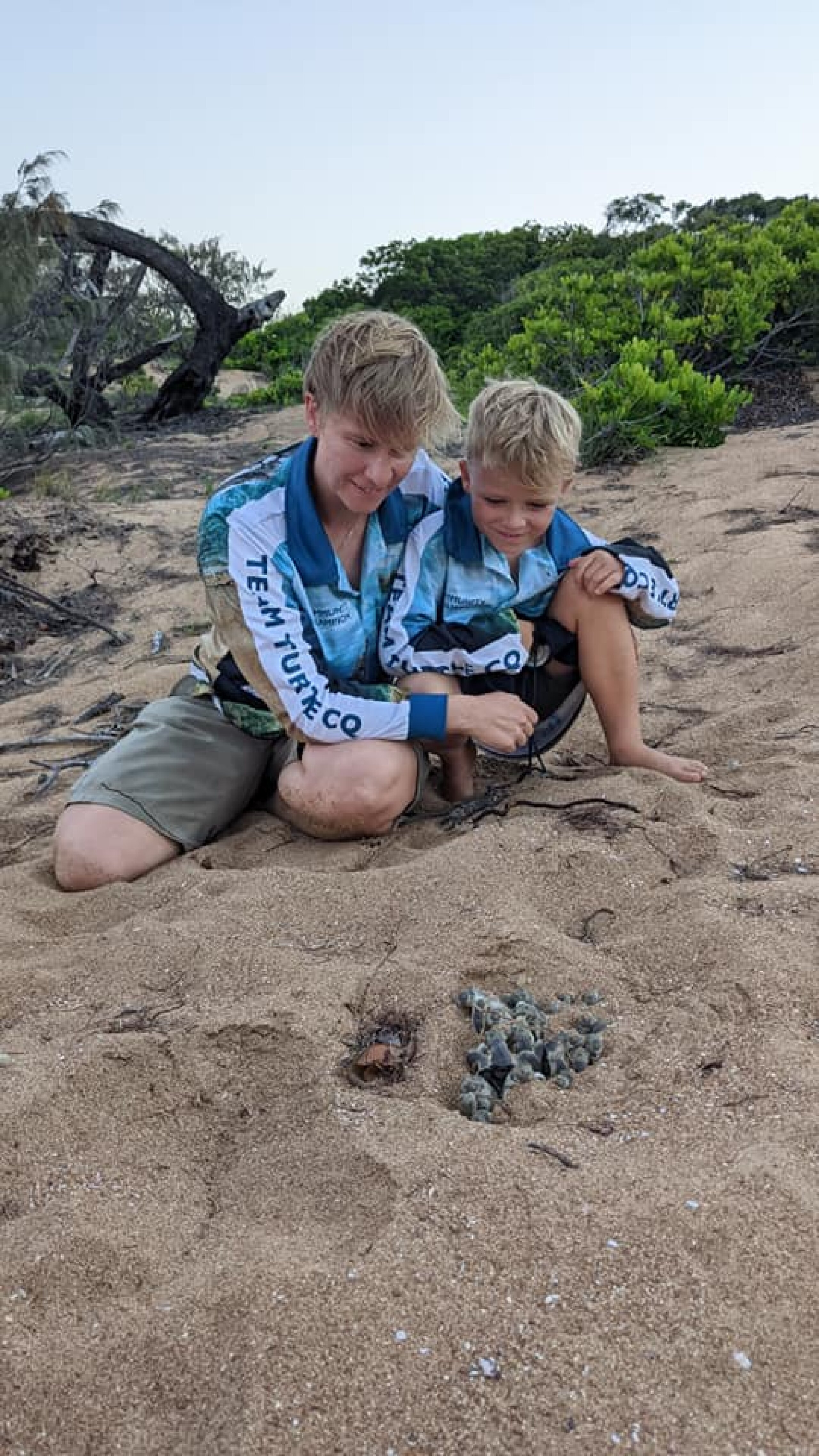 Two volunteers watch turtles hatching on the beach.