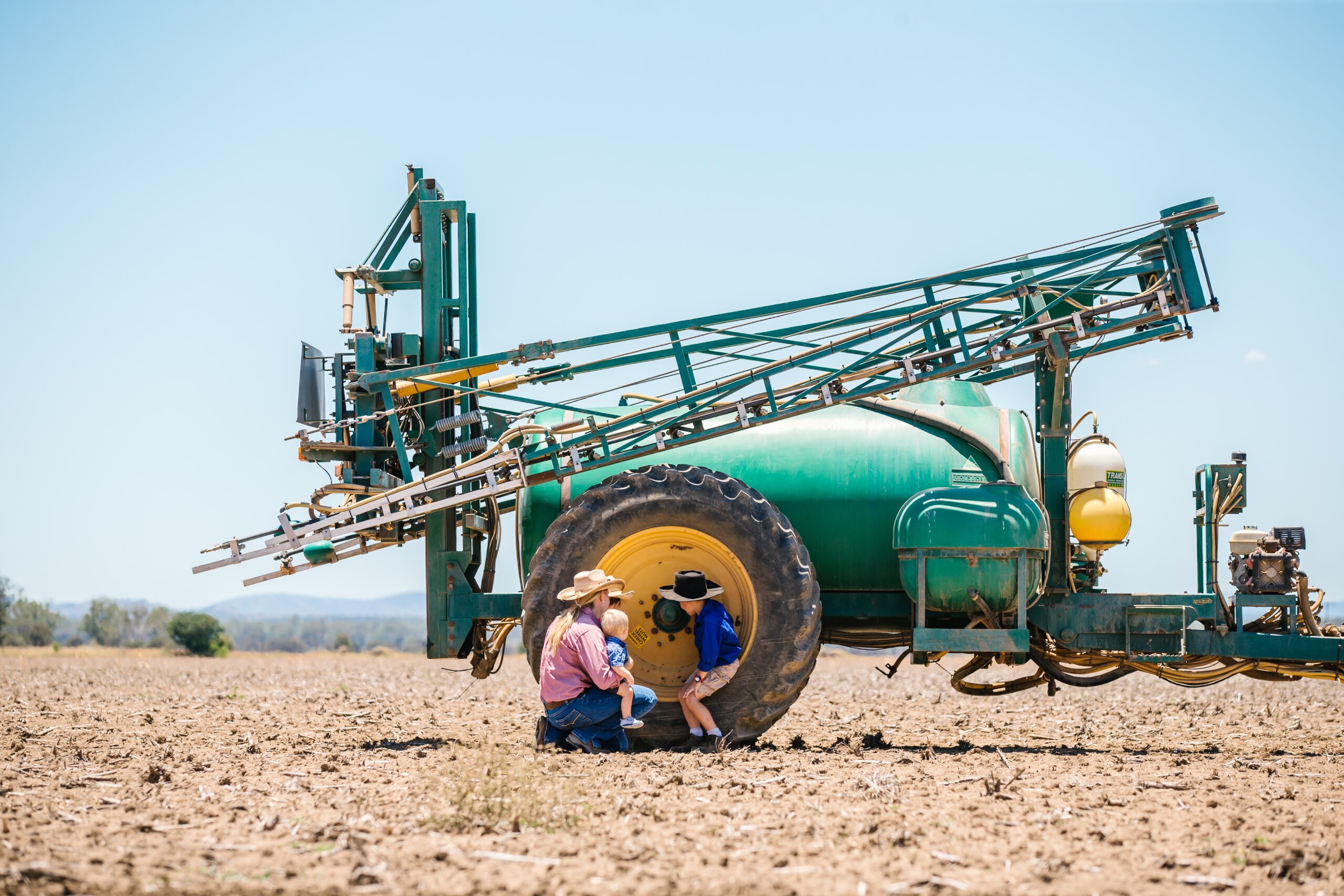A land manager kneeling next to farming machinery together with her two children