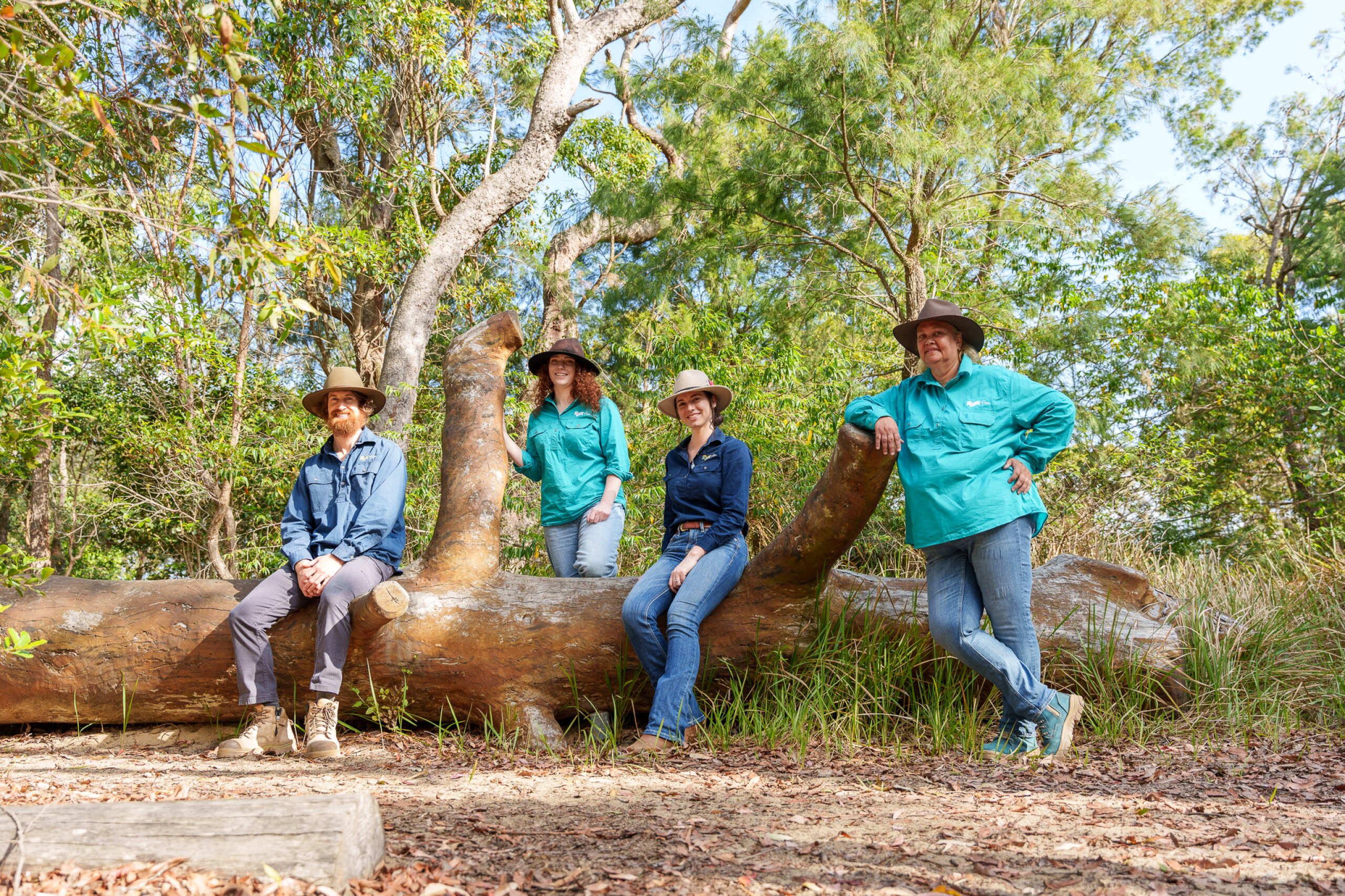 Four FBA staff members are sitting on and leaning against a log on Mt Archer