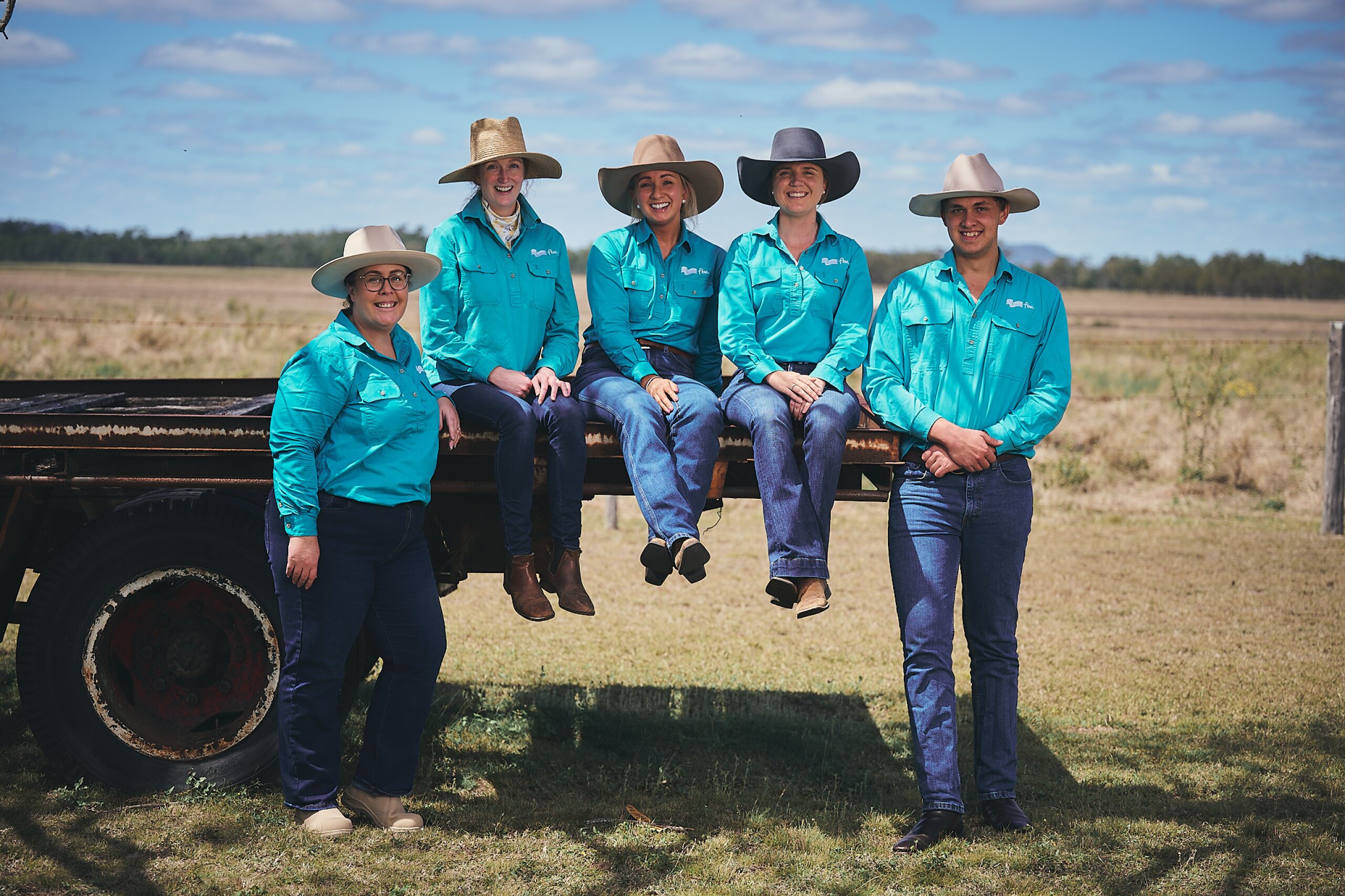 Five FBA staff member leaning on or sitting on the back of a truck smiling at the camera