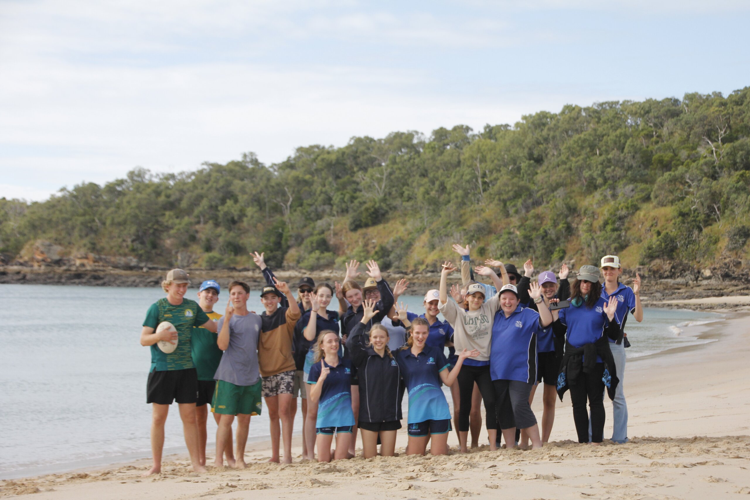 A group of school students smile and raise their hands on a beach at the Capricorn Coast
