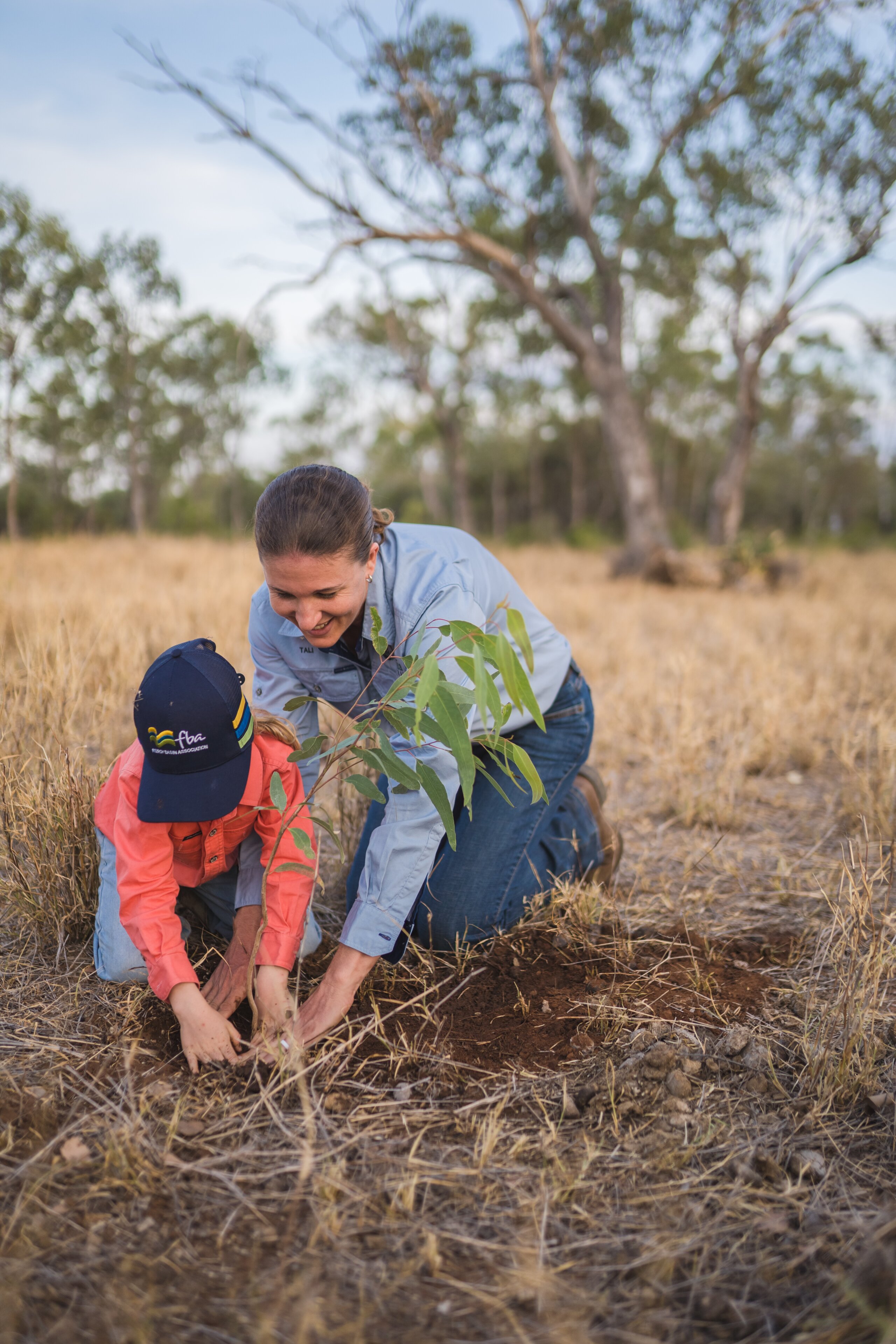 A woman helps her daughter plant a tree.