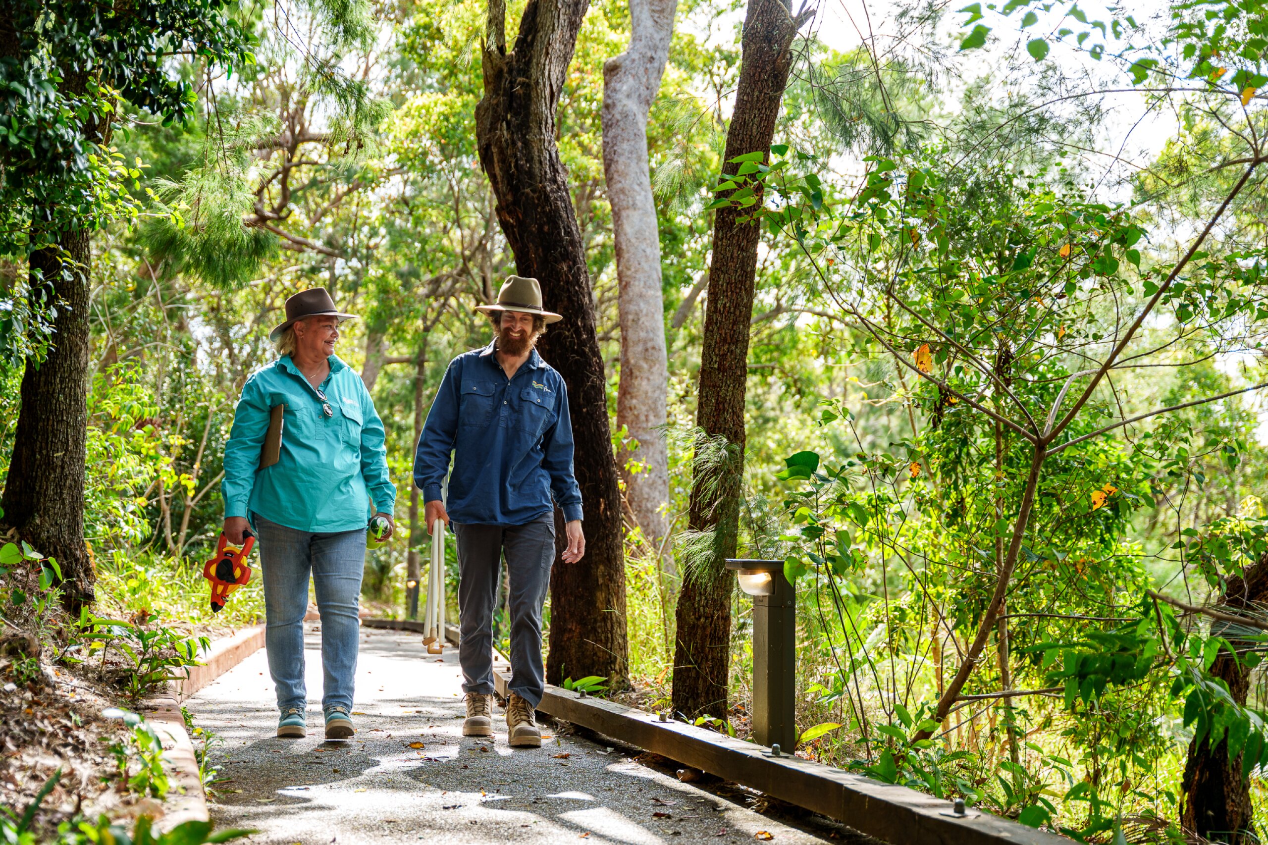 Two FBA staff walk along a path on Mt Archer holding measurement apparatus.