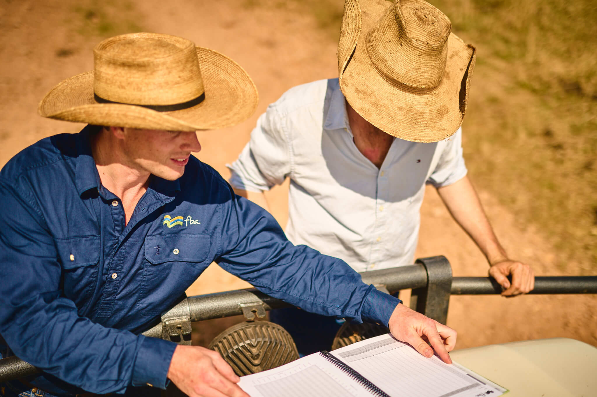 Two FBA staff members look over a document on the bonnet of a car.